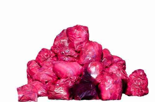 A pile of tightly packed, bright pink plastic rubbish bags arranged on a flat surface, with some bags stacked on top of others and others leaning against the pile. The bags have a glossy finish, with visible creases and folds, and appear to contain waste materials. The background is plain and white, emphasizing the vibrant colour of the bags. This image represents typical waste items that a rubbish removal service like Business Waste Removal Canary Wharf might handle, situated in an urban environment near Canary Wharf. The overall scene is well-lit, highlighting the shiny surface and irregular shapes of the bags, which are common in waste collection and disposal contexts within the area.