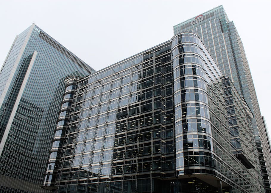 A modern multi-storey glass office building with curved, reflective facade panels presenting a sleek, contemporary appearance, situated among other high-rise structures in an urban setting. The buildi